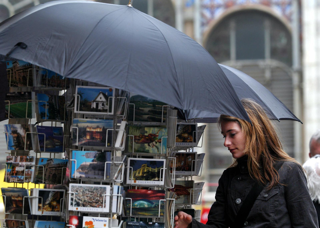 Una turista contempla unas postales protegidas por paraguas debido a la inestabilidad del tiempo. EFE/Kai Försterling/Archivo